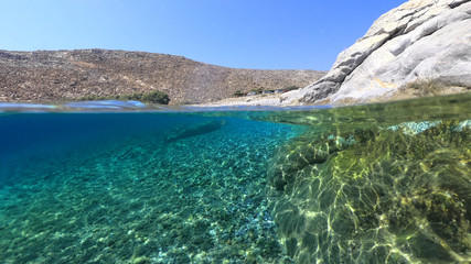 Above and below underwater photo of crystal clear turquoise pebble beach of Kaminakia, Astypalaia island, Dodecanese, Greece