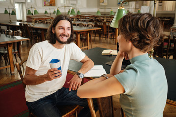 Fototapeta premium Young handsome male student joyfully talking with friend during study break in library of university