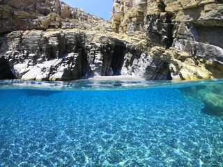 Above and below underwater photo of crystal clear sea paradise rocky seascape full of caves beach...