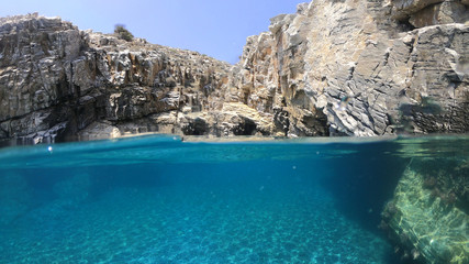 Above and below underwater photo of crystal clear sea paradise rocky seascape full of caves beach...