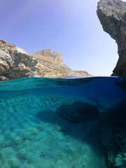 Above and below underwater photo of crystal clear sea paradise rocky seascape full of caves beach...