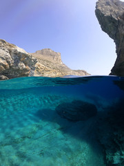 Above and below underwater photo of crystal clear sea paradise rocky seascape full of caves beach of Mouros, Amorgos island, Cyclades, Greece