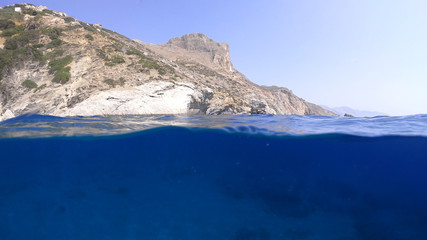 Above and below underwater photo of crystal clear sea paradise rocky seascape full of caves beach of Mouros, Amorgos island, Cyclades, Greece