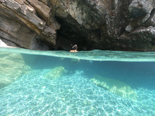 Above and below underwater photo of crystal clear sea paradise rocky seascape full of caves beach...