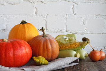 Autumn pumpkins and other vegetables on a wooden thanksgiving table, white brick backdrop, selective focus