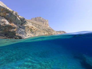 Fototapeta premium Above and below underwater photo of crystal clear sea paradise rocky seascape and small chapel of Agia Anna just next to iconic Hozoviotissa Monastery, Amorgos island, Cyclades, Greece