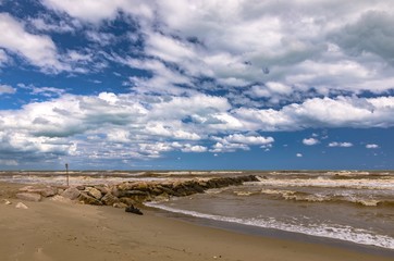 Seascape with cloudy sky, rocks and beached trunk