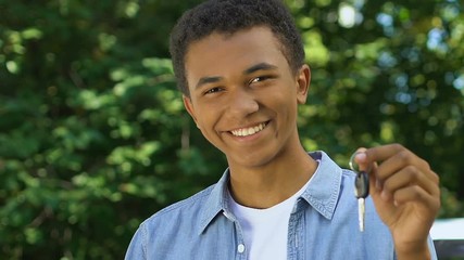Happy black teenage boy showing auto keys to camera, getting driver license