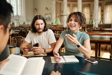 Young casual students with book emotionally discussing project together in library of university