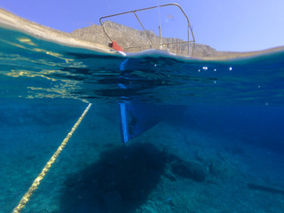 Above and below underwater photo of colourful traditional fishing boat in crystal clear turquoise sea of Astypalaia island, Dodecanese, Greece