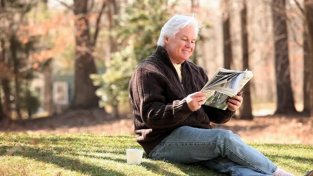 Smiling senior Caucasian man drinking coffee and reading newspaper on lawn
