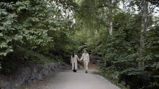 Wide shot of a young happy travelling couple walking a small road in a Stockholm park.