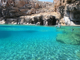 Above and below underwater photo of crystal clear sea paradise rocky seascape full of caves beach...