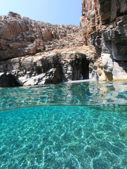 Above and below underwater photo of crystal clear sea paradise rocky seascape full of caves beach...