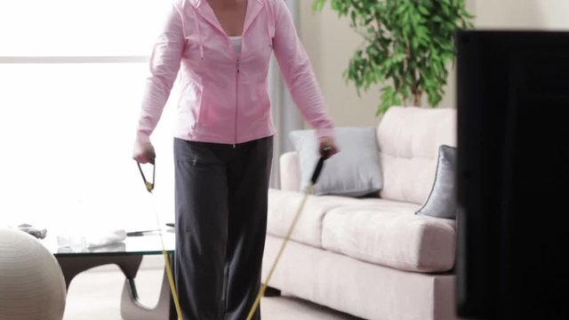 Asian woman exercising with resistance bands while watching television