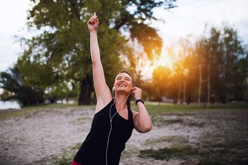Young woman in sport wear enjoys and smiles listening music with earphones
