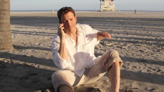 Caucasian man sitting on sand with cell phone