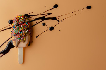 Orange popsicle with chocolate glaze with black topping on pastel light peach background.