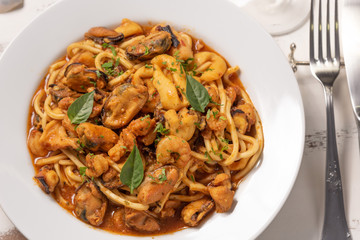 Pasta with sea fruit in white plate on a white wooden background, soft light. Spaghetti ai frutti di mare, seafood mediterranean gastronomy