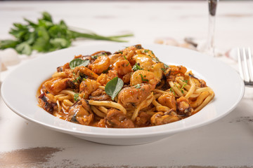 Pasta with sea fruit in white plate on a white wooden background, soft light. Spaghetti ai frutti di mare, seafood mediterranean gastronomy