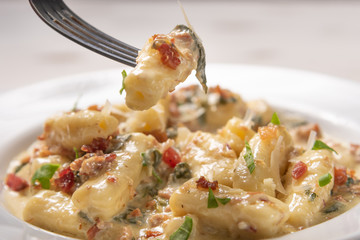 Penne pasta with carbonara sauce in white plate on wooden white background, soft light, angle view. Italian food