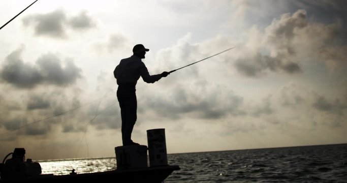 Silhouette of Caucasian fisherman fly fishing on skiff boat