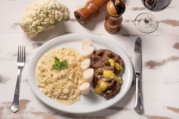 Risotto with filet mignon. Risoto and beef with capers and mustard in a white plate on wooden white background. Soft light. Italian food.