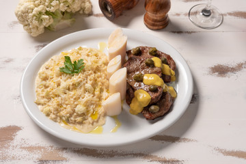 Risotto with filet mignon. Risoto and beef with capers and mustard in a white plate on wooden white background. Soft light. Italian food.