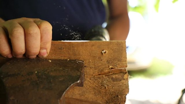 A carpenter drills a hole in a board with an electric drill, outdoors, close-up