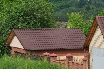 Obraz premium brown roofs of buildings with tiles over a fence in green vegetation