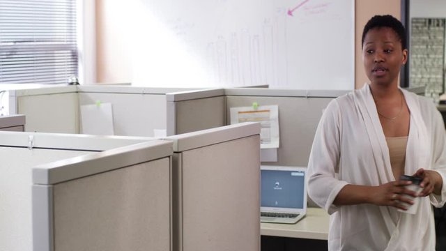 African American businesswoman standing and talking over office cubicle with coffee