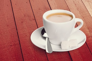 Cup of coffee and scattered coffee beans on wooden background