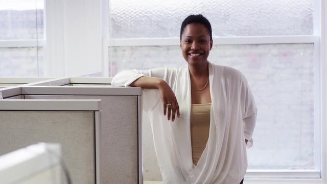 Smiling African American businesswoman leaning on cubicle wall