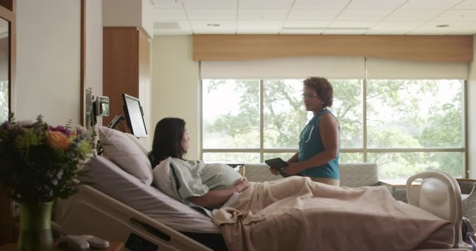Doctor with digital tablet talking to expectant mother in hospital room