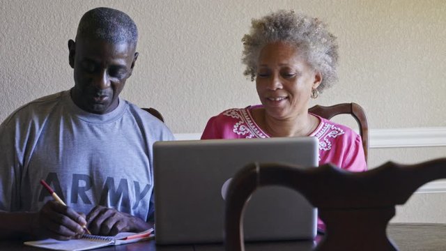 Retired Black military man and wife researching benefits on laptop