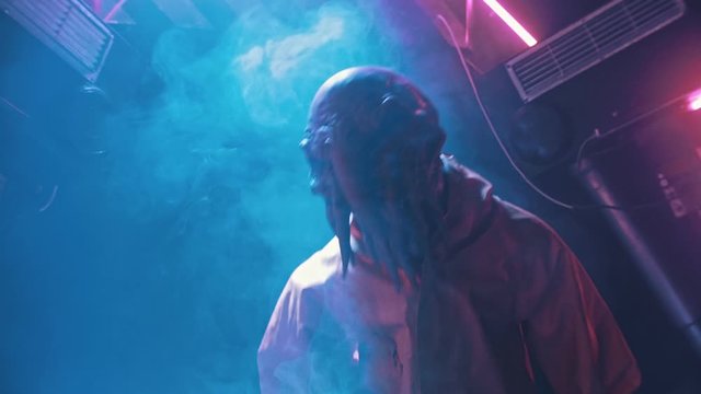 An alien with tentacles in the lower face walking on the secret laboratory in worker clothes