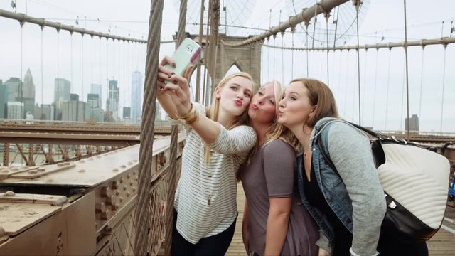 Caucasian women posing for cell phone selfies on bridge