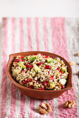 Salad of germinated buckwheat, avocado, walnut and pomegranate seeds in clay plate on white wooden background.