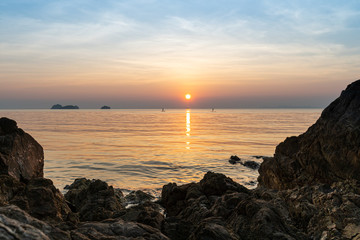 Couple of paddle boarders in the sea against a tropical sunset and rocks on the beach 