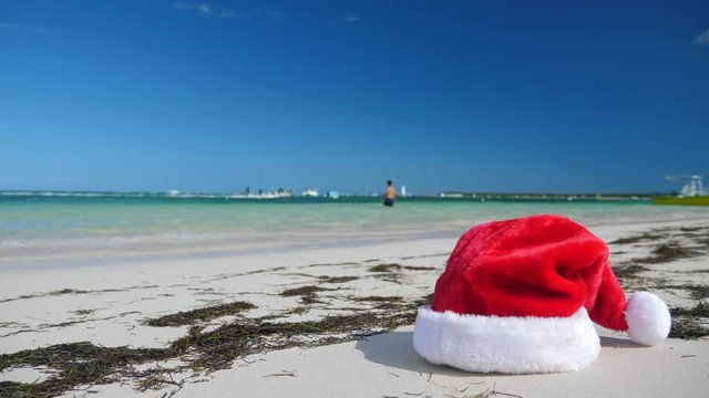 Christmas Santa Claus hat on tropical sandy beach with calm waves. Winter holidays. New Year celebration on caribbean island