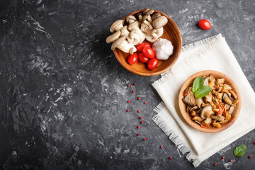 Fried oyster mushrooms with tomatoes in wooden plate on black concrete background. top view.