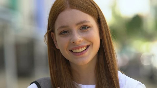 Attractive red-haired teenager smiling on camera, natural beauty, femininity