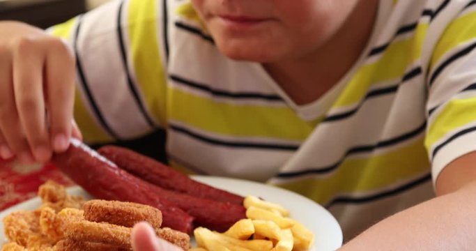 Portrait ofa caucasian teenage boy sitting at home and eating unhealthy foods