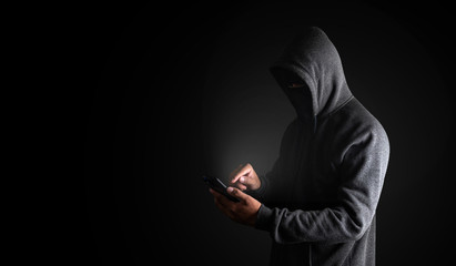Hacker Using Smartphone. Men in black clothes with hidden face looks at smartphone screen on black...