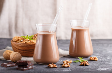 Organic non dairy walnut chocolate milk in glass and wooden plate with walnuts on a black concrete background.