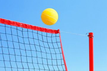 volleyball on the beach, net and yellow ball on blue sky background.
