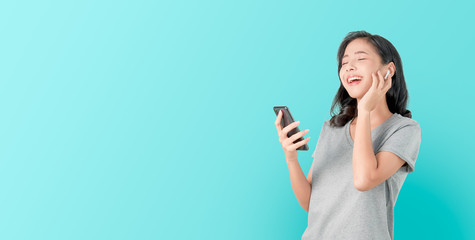 Asian women of happy smiling are listening to music from white headphones. And using hands touch to use various functions, happy mood on blue background.