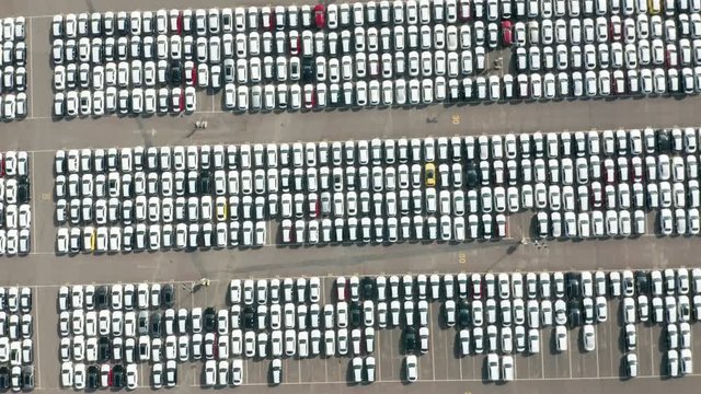 Aerial top down view of automaker car lot showing vehicles lined up parked close to each other. Circle aerial shot.