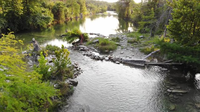 Flying about 20 feet above river near recreational swimming area at sunset; man made dams visible in river. - Aerial footage of the Blanco river in Wimberly, TX