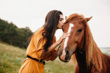 Outdoor shot of a attrative young girl kissing a horse on a filed.